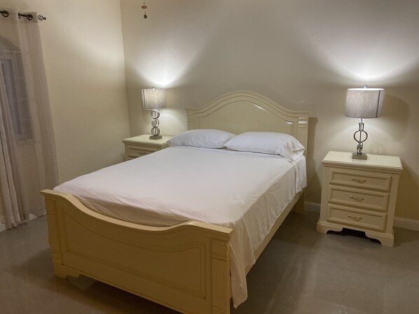 A bedroom with a bed, two bedside tables with lamps, a nightstand, and a curtain.