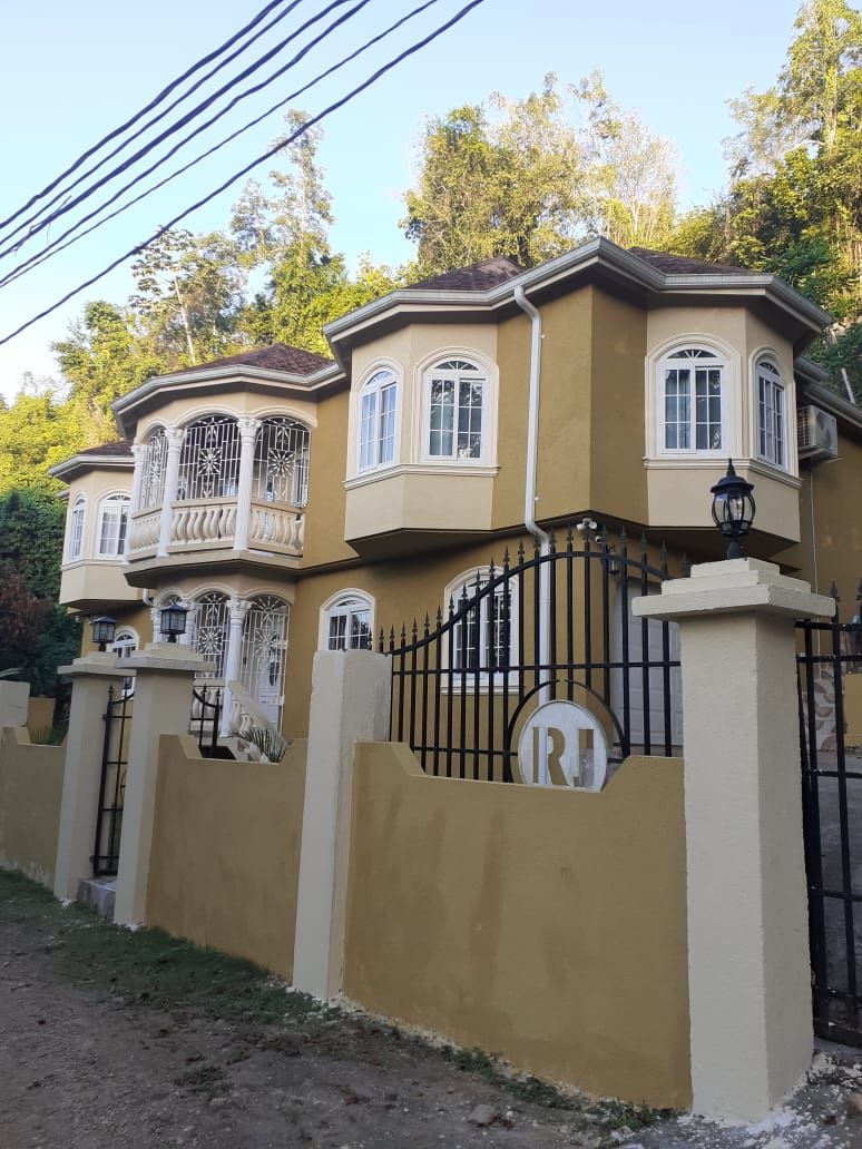 A large, multi-story house with a prominent balcony, a gated entrance, and a well-maintained garden.
