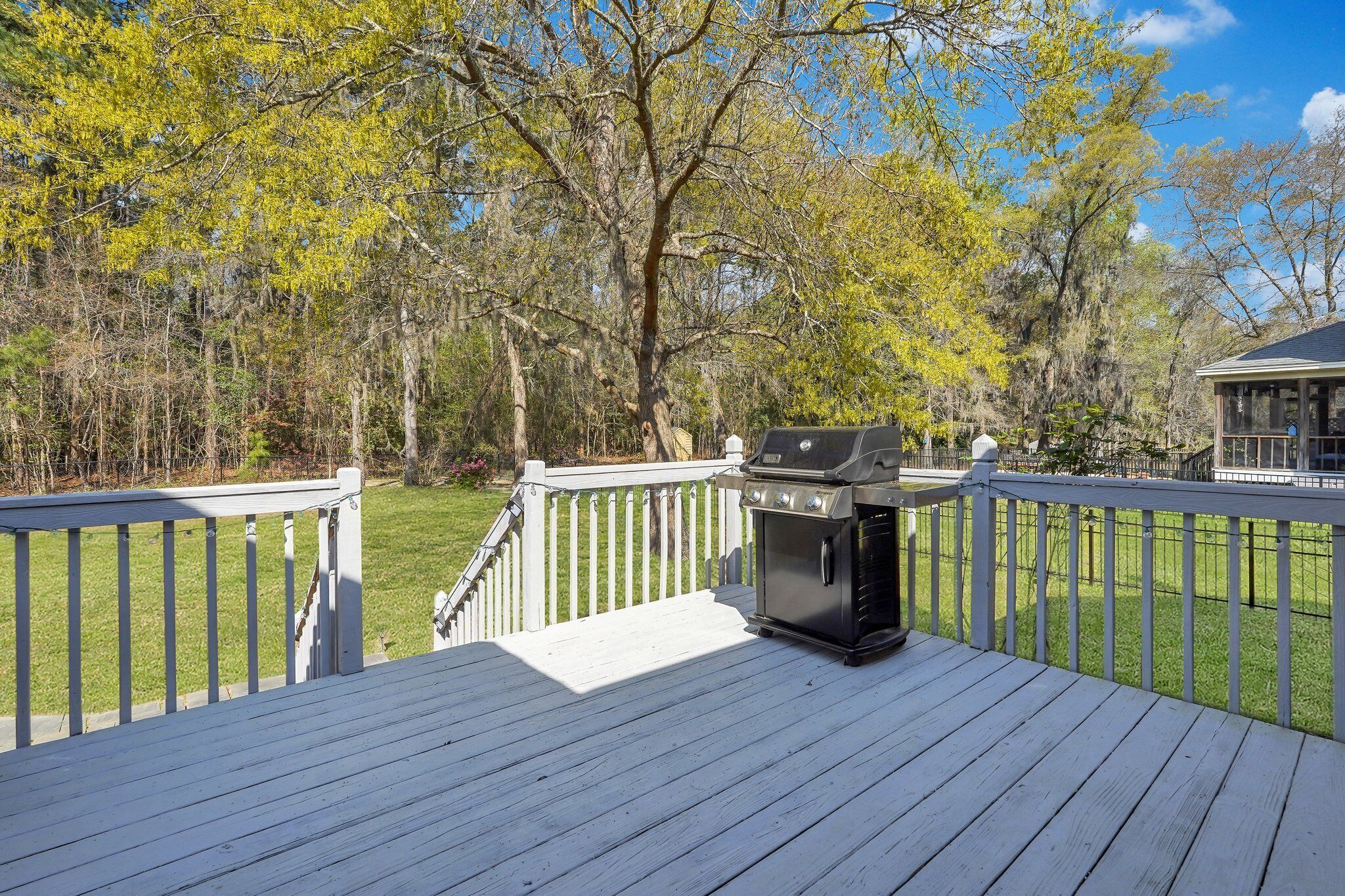 A deck with a barbecue grill, surrounded by a white fence and trees.