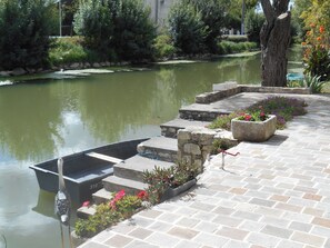A stone pathway leading to a boat docked by a calm river, with steps and flower planters along the way.