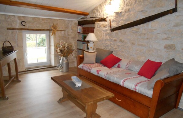 A cozy living room with a wooden sofa, a coffee table, a bookshelf, and a stone wall.