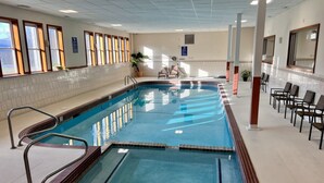 Ein langer, überdachter Schwimmbereich mit markierten Bahnen, einem Rettungsschwimmerstuhl und einer Sitzgelegenheit mit Stühlen.