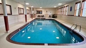 Una piscina interior con paredes de azulejos, un cartel de prohibición de clavados y una escalera que sube a un nivel superior.