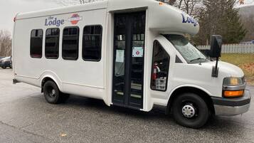 Un autobús blanco con los logotipos 'The Lodge' y 'Lodge', una puerta delantera y ventanas.