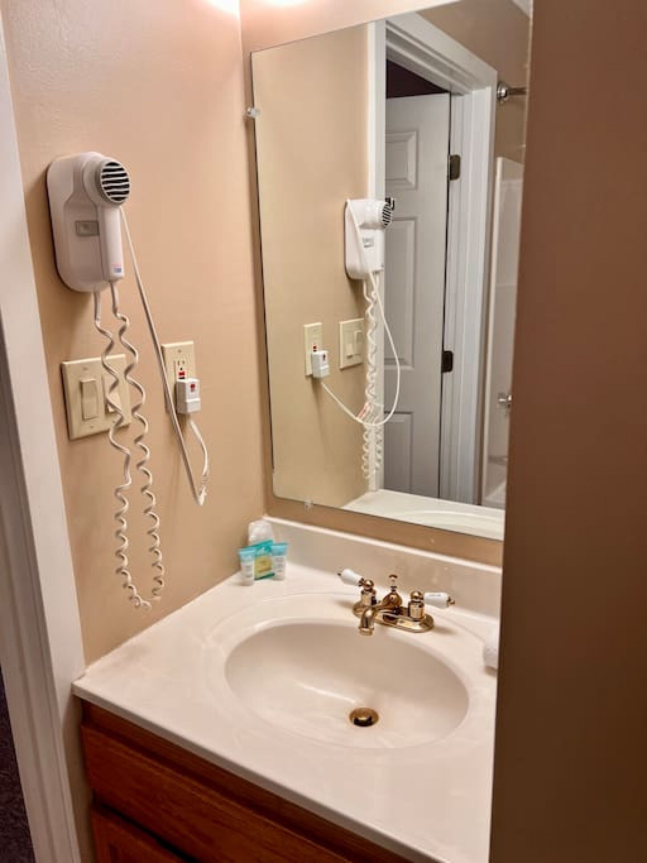 A bathroom with a sink, a mirror, and two hair dryers plugged in.