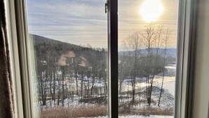 Une fenêtre donnant sur un paysage enneigé, avec des arbres et une colline.