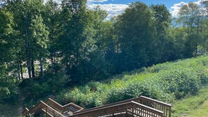 A wooden deck with a railing, surrounded by dense green foliage and trees under a clear blue sky. - Top 5 Pct Hotel Room with King Bed and Stunning Loon Mountain Views (Lincoln)