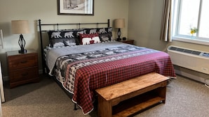 A bedroom with a bed, two bedside tables, a bench, a window with curtains, a wall-mounted heater, and a framed picture on the wall. - Top 5 Pct Hotel Room with King Bed and Stunning Loon Mountain Views (Lincoln)