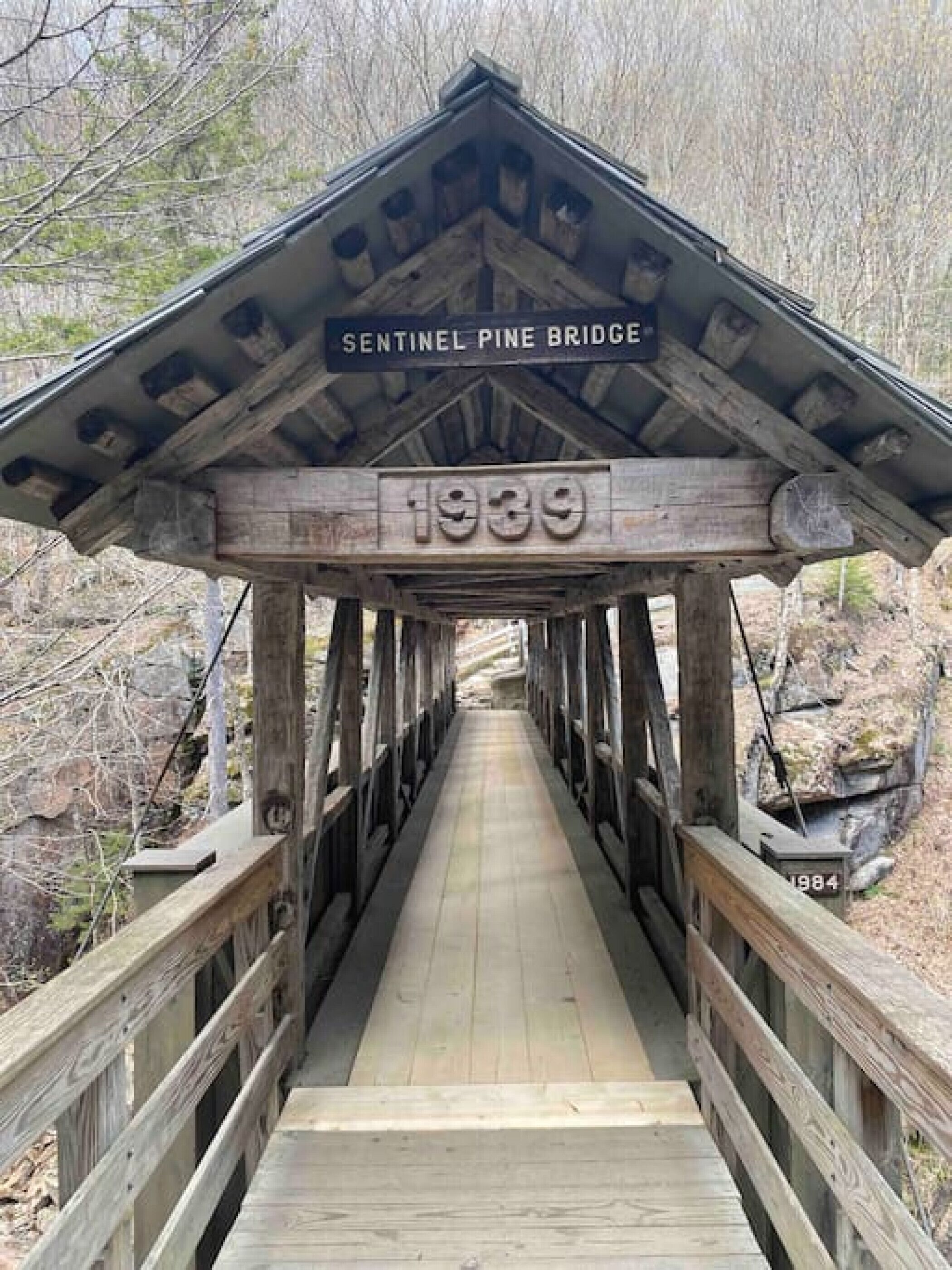 Eine Holz-Fußgängerbrücke mit einem Schild, auf dem 'Sentinel Pine Bridge 1939' steht, und einem Jahreszeichen '1984'.