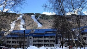 Un hotel con techo azul, una pista de esquí al fondo y nieve en el suelo.