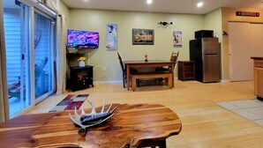 Un soggiorno con un tavolo da pranzo in legno, una televisione e un angolo cottura con frigorifero.