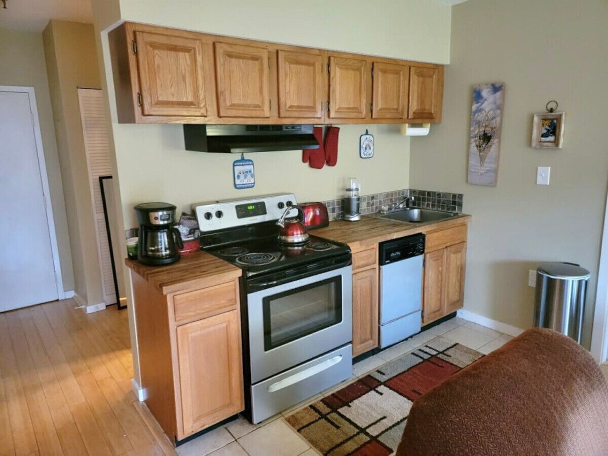 A compact kitchen with wooden cabinets, a stove, a dishwasher, and a coffee maker.