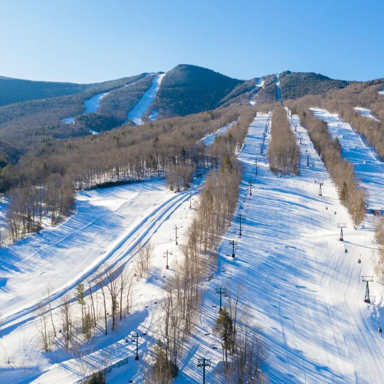 A snow-covered ski slope with ski lifts and a mountain backdrop.
