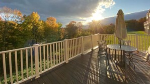Una terrazza con tavolo e sedie, affacciata su un paesaggio rigoglioso con alberi e un edificio sullo sfondo.