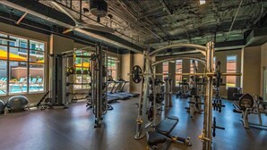 A gym with various exercise equipment, a bench, and a view of a pool through large windows.