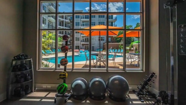 A gym with exercise equipment and a view of a swimming pool through large windows.