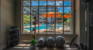 Un gimnasio con equipo de ejercicio y vistas a una piscina a través de amplios ventanales.