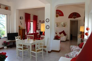 Sala de estar com área de jantar, cortinas vermelhas e decorações tradicionais nas paredes.