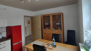 A compact kitchen with white cabinets, a red refrigerator, and a wooden dining table with a placemat. - Quietly located vacation apartment in Reichshof Eckenhagen (Reichshof)