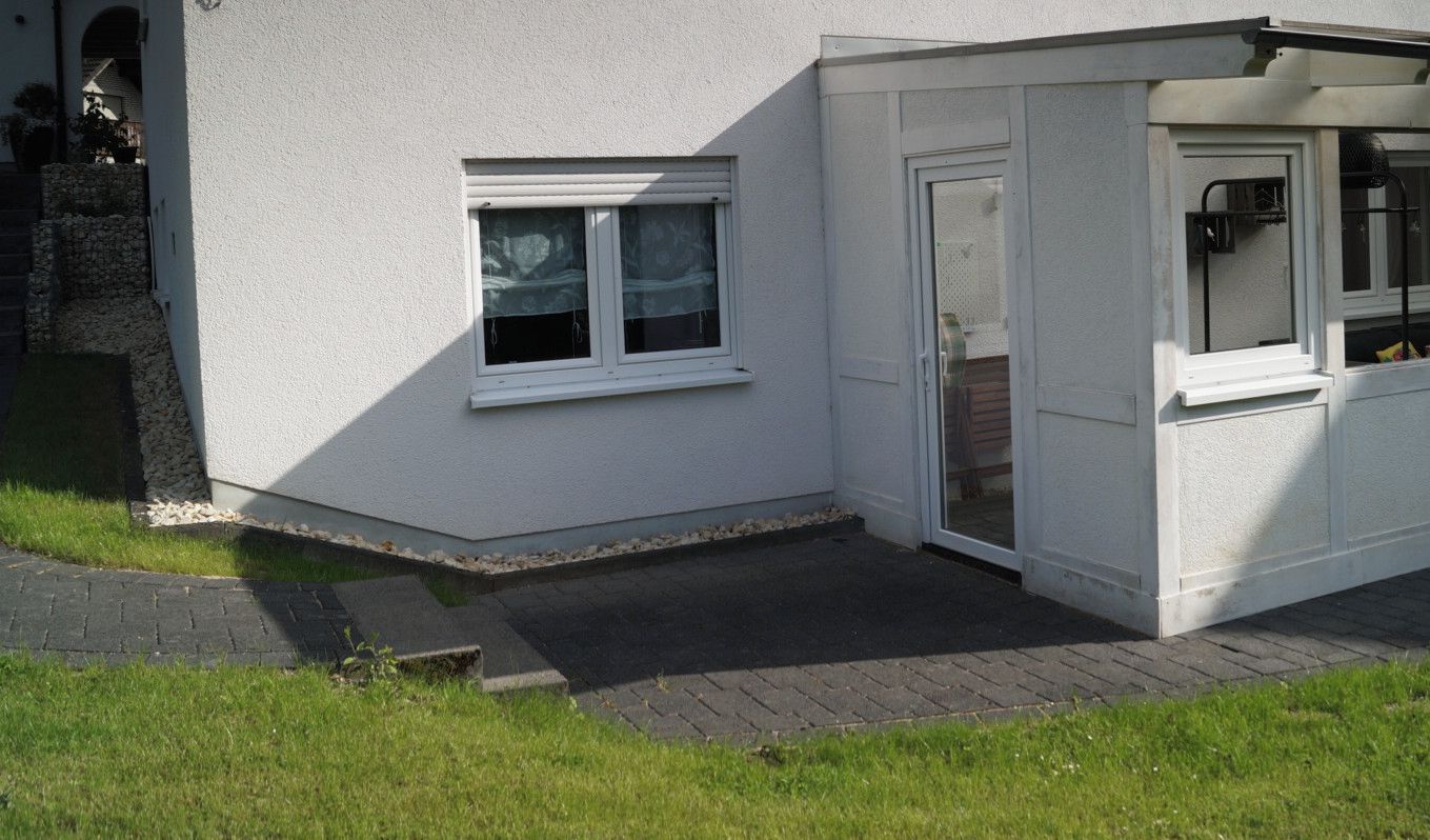 Ein weißes Gebäude mit einer Veranda, einem kleinen Fenster und einer Tür.