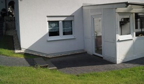 Un bâtiment blanc doté d’un porche abrité, d’une petite fenêtre et d’une porte.