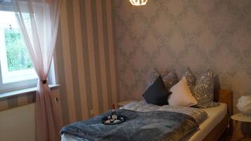 Ein Schlafzimmer mit Bett, Vorhängen, einer Hängelampe, einem kleinen Tisch und einer Wand mit Muster.