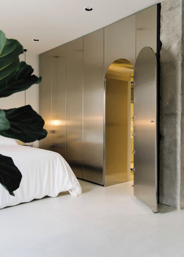 A modern bedroom with a bed, a large plant, and a wardrobe with a gold interior.