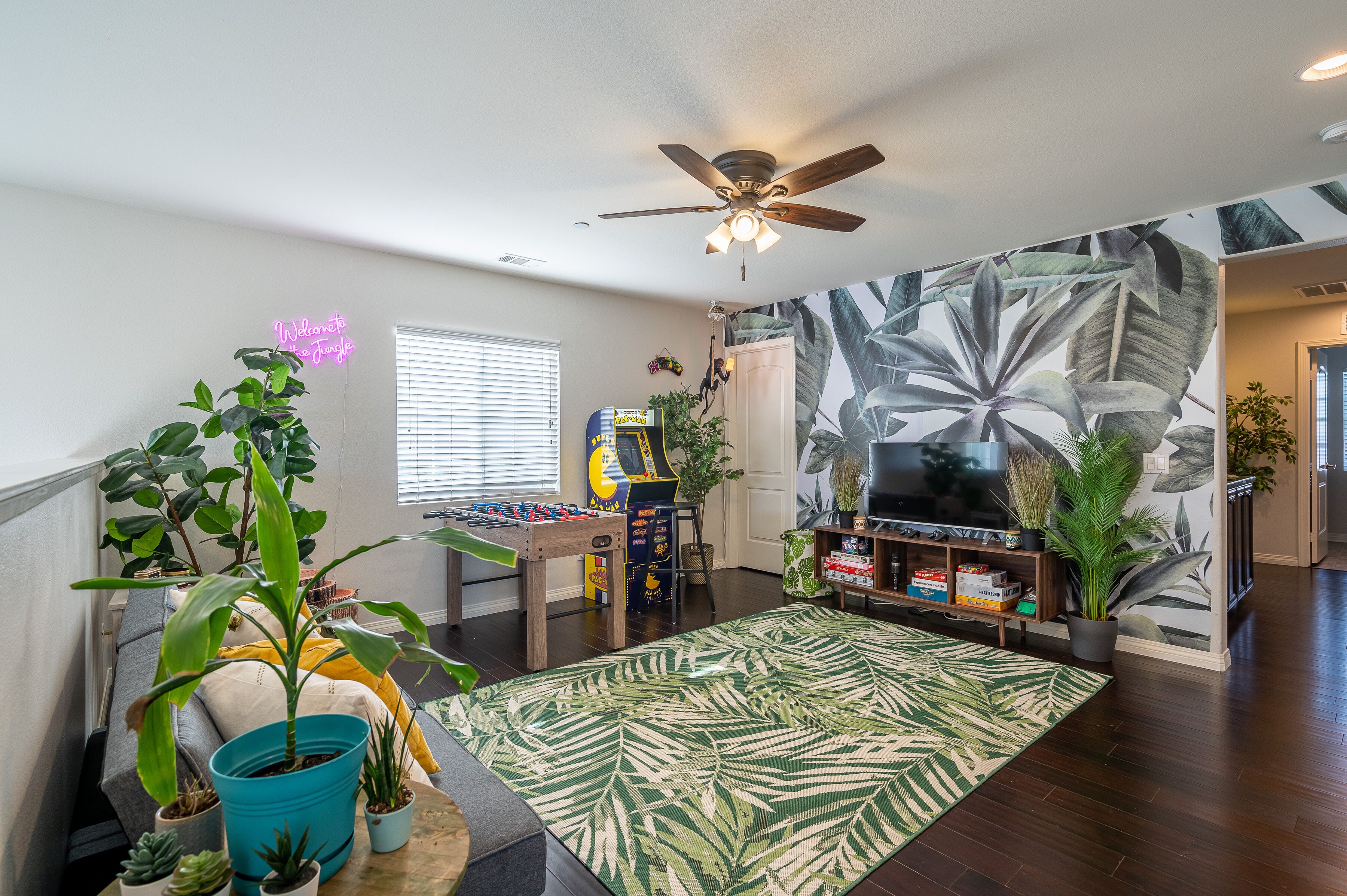 A living room with a foosball table, a ceiling fan, and a large plant wall.