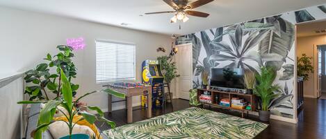 A living room with a foosball table, a ceiling fan, and a large plant wall.