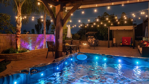 Een terras buiten met een hottub, lichtjes en zitplaatsen.