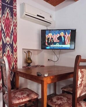 A dining area with a wooden table and four chairs, a flat-screen TV mounted on the wall, and an air conditioning unit. - Single Room with Private Bathroom (Buxoro)