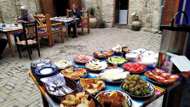 An outdoor dining area with a variety of food items on a table, surrounded by stone walls and traditional doors. - Single Room with Private Bathroom (Buxoro)