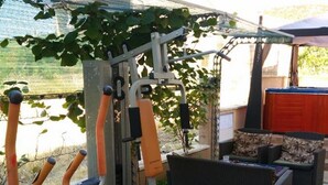 Une salle de sport en plein air équipée de matériel d’exercice, un espace de repos couvert et une vue sur un jardin.