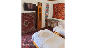 A hotel room with two beds, a television, and traditional patterned rugs.