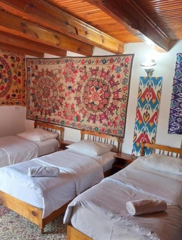 Ein Zimmer mit drei Holzbett, einem großen Blumenwandteppich und einem gemusterten Wandbehang.