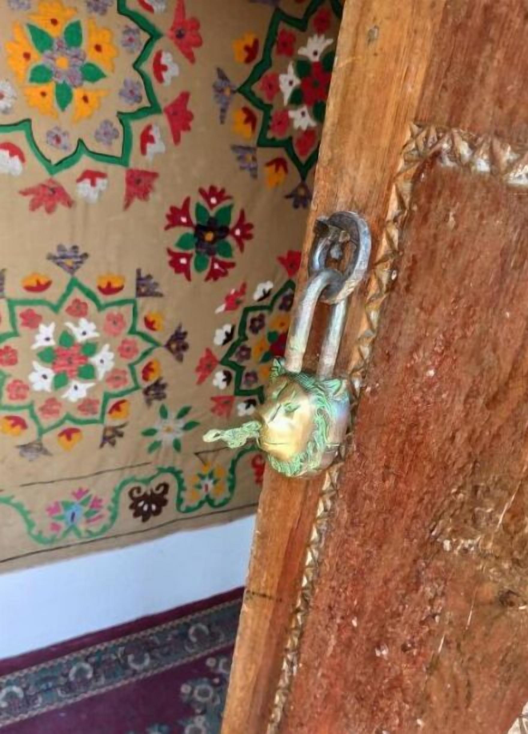 A wooden door with a brass padlock and a colorful floral-patterned wall behind it.