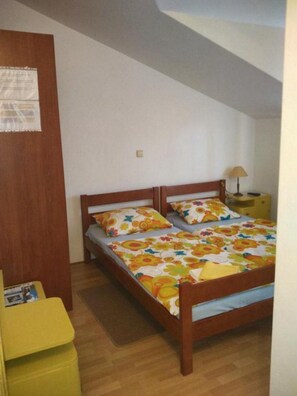 Une chambre avec un lit en bois, une literie aux motifs floraux colorés, une table de chevet avec une lampe et une petite table jaune.