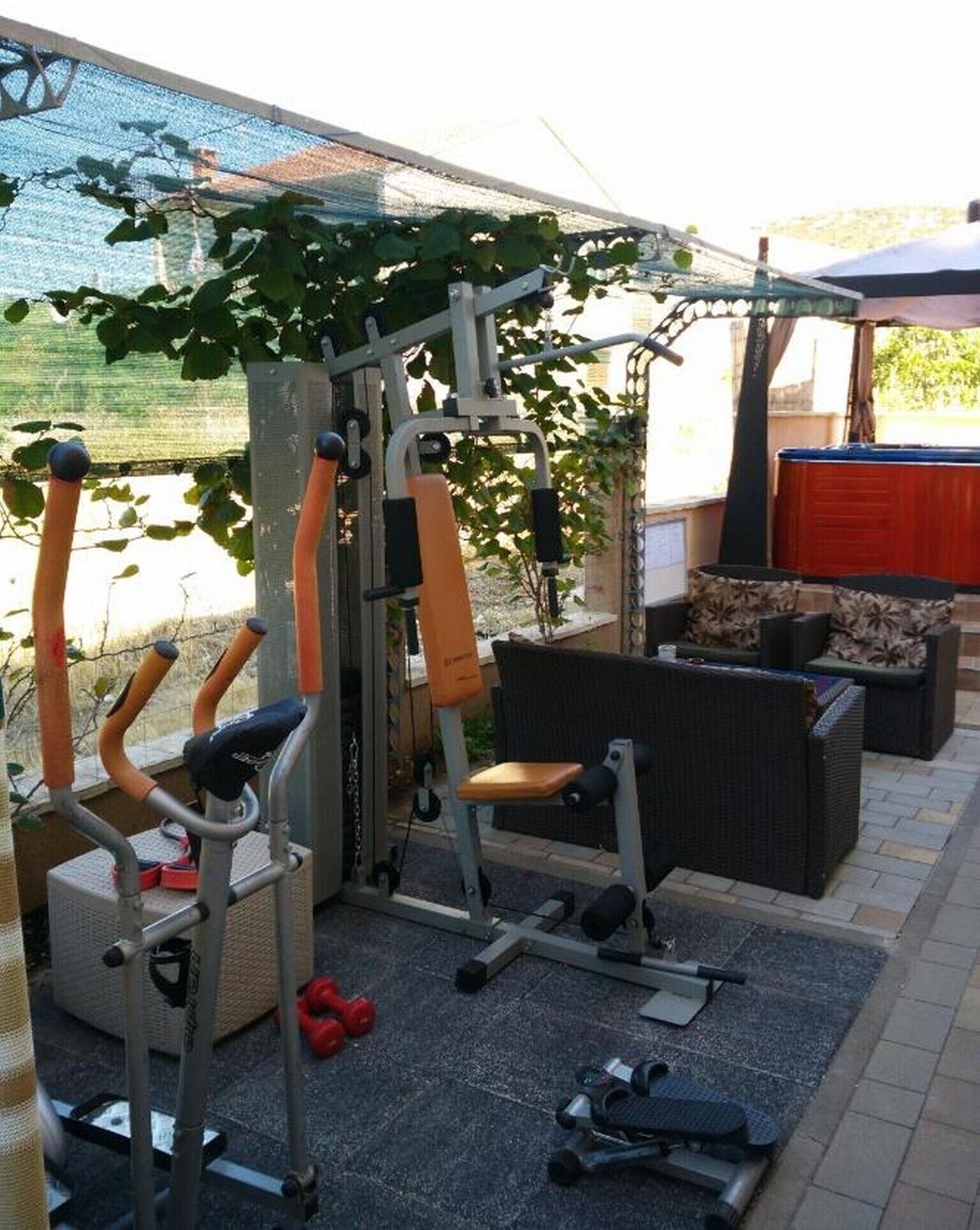 Una palestra all'aperto con attrezzature per esercizi, un'area relax e un portico coperto.