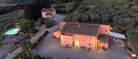 A large villa with a tiled roof, surrounded by a gravel driveway and potted plants.