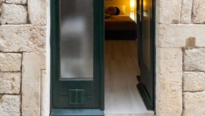 Une porte qui donne sur une pièce où se trouvent un lit, une lampe et une étagère fixée au mur.