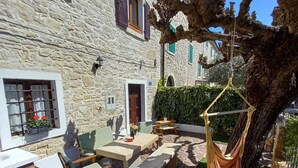 Edificio de piedra con un patio amueblado, que incluye mobiliario exterior y una silla colgante.