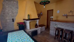 Un comedor con una mesa cubierta por un mantel de lunares, una chimenea de piedra y taburetes de bar de madera.
