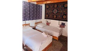A room with two wooden beds, a patterned tapestry, and a decorative wall hanging. - Triple Room with Private Bathroom (Buxoro)