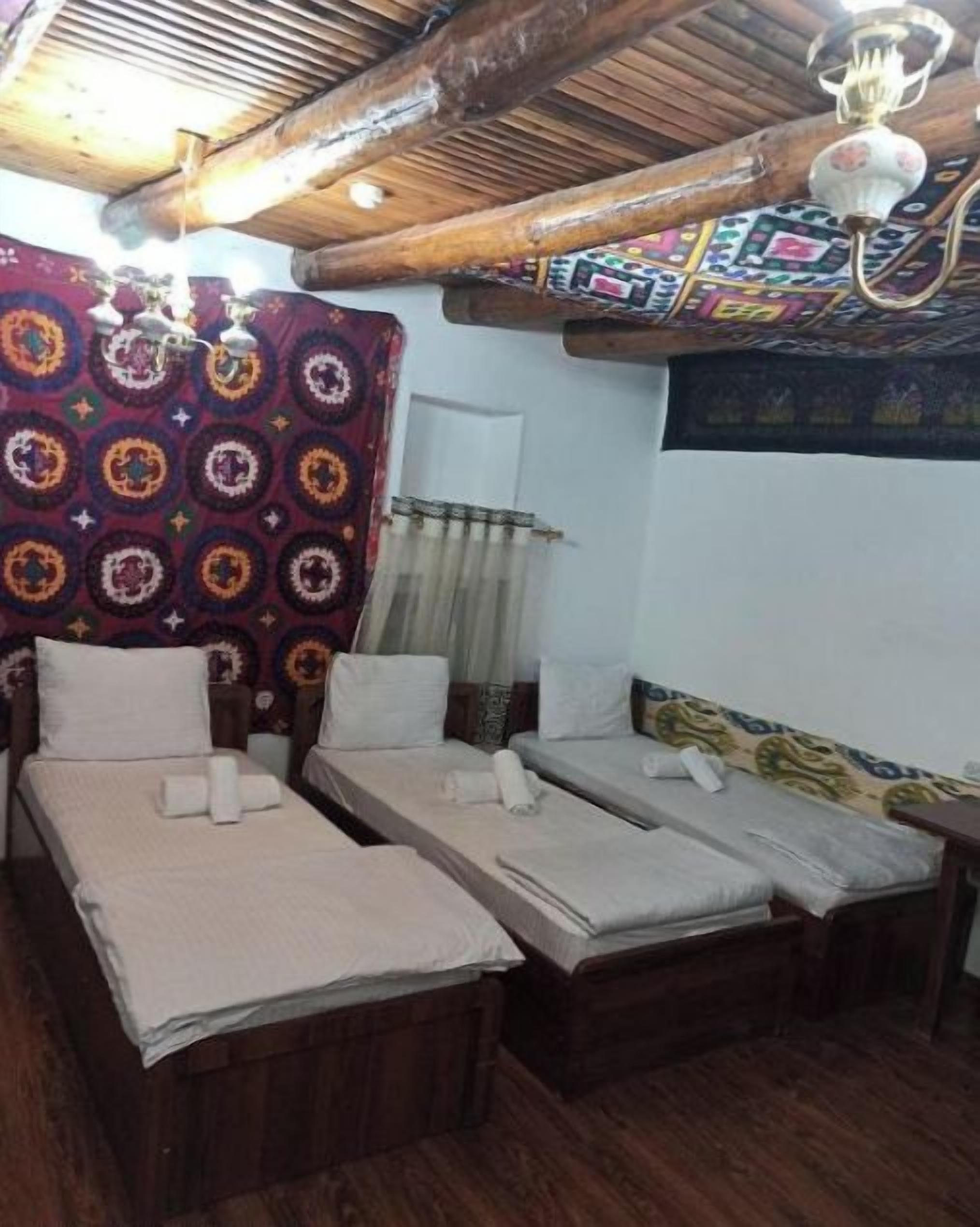 A room with three wooden beds, a patterned curtain, and a ceiling with exposed beams and a chandelier.