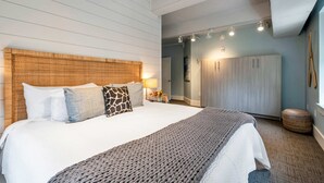 A bedroom with a large bed, a wooden headboard, a grey knitted throw, a wardrobe, and a small round ottoman. - Honky Tonk Suite/6 BR/3600sqft, Walkto Broadway (Nashville)