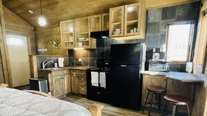 A compact kitchen with wooden cabinets, a black refrigerator, and a small dining area with stools. - Historic Westcliffe Outpost Loft (Westcliffe)