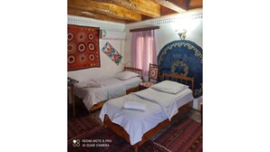 A room with two single beds, a wooden ceiling, and a patterned wall hanging.