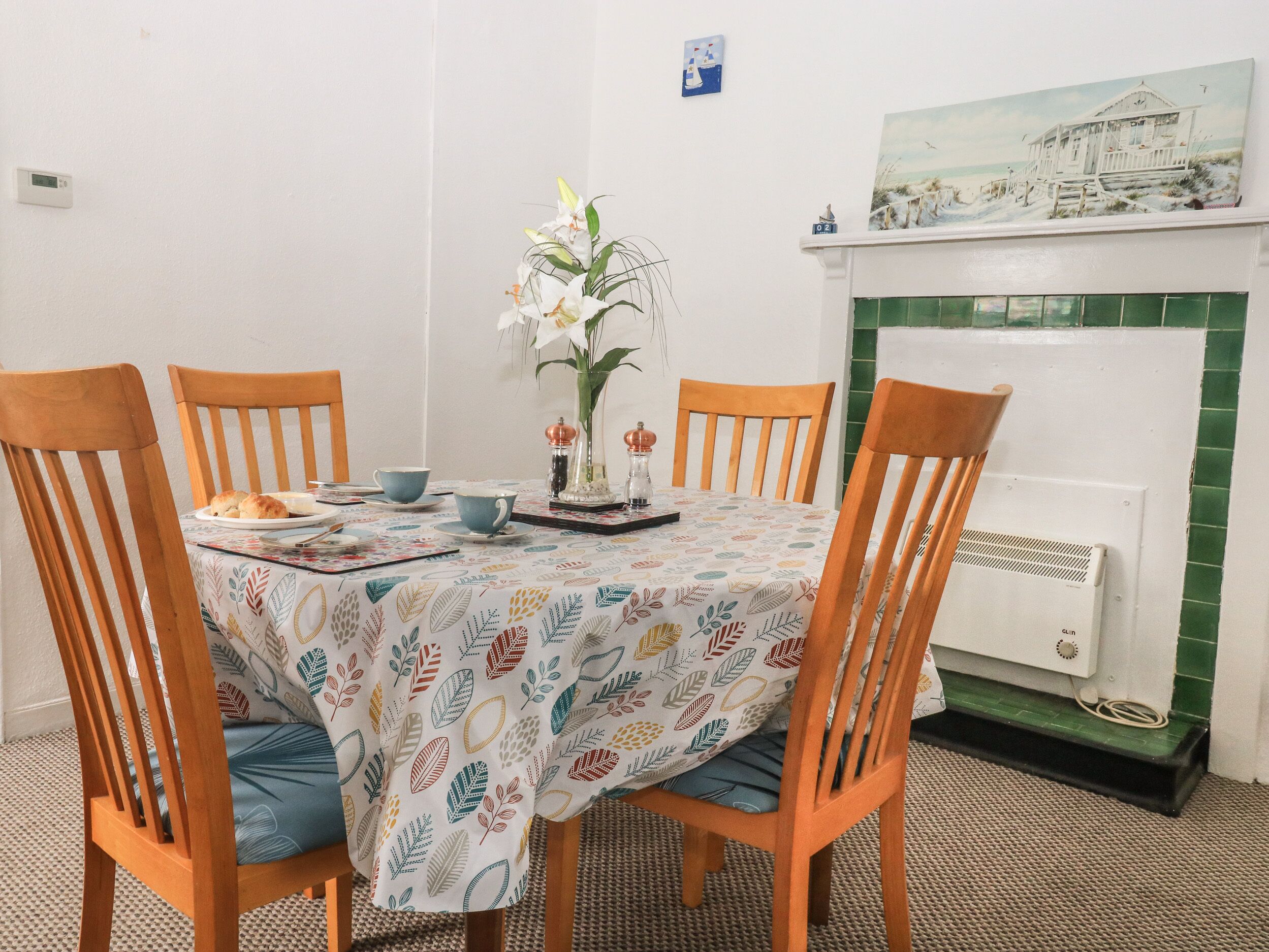 A dining area with a table set for four, surrounded by wooden chairs. A vase with white flowers is placed in the center.