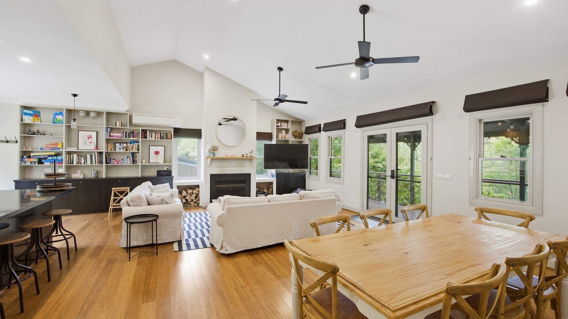 A spacious living area with a wooden dining table, sofas, and a kitchen area with a TV and fireplace.