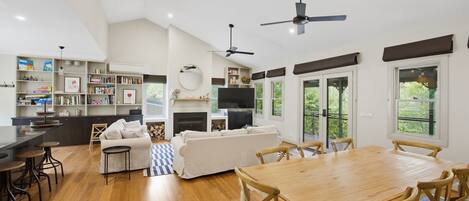 A spacious living area with a wooden dining table, sofas, and a kitchen area with a TV and fireplace.
